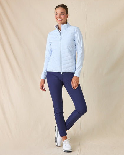 Women's Ida Hybrid Jacket in Lake, full length side view on model featuring a light blue hybrid jacket with quilted puffer front body and stretch knit sleeves, paired with navy pants and white golf shoes