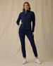 Women's Ida Hybrid Jacket in New Indigo, front full-length view featuring a full-zip closure, horizontal quilted front body, stretch side panels, and hand in side pocket paired with navy pants and white shoes