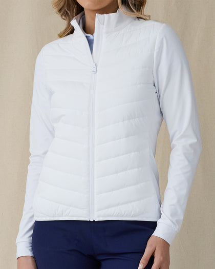 Women's Ida Hybrid Jacket in White, front close-up view featuring a full-zip closure, horizontal quilted chest and front body, and stretch side panels worn over a light blue polo
