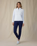 Women's Ida Hybrid Jacket in White, front full-length view featuring a full-zip closure, horizontal quilted front body, and stretch side panels paired with navy pants and white shoes worn over a light blue polo