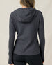 The back view of a woman modeling a dark heather gray textured hooded sweater and black pants, against a plain light beige studio background.