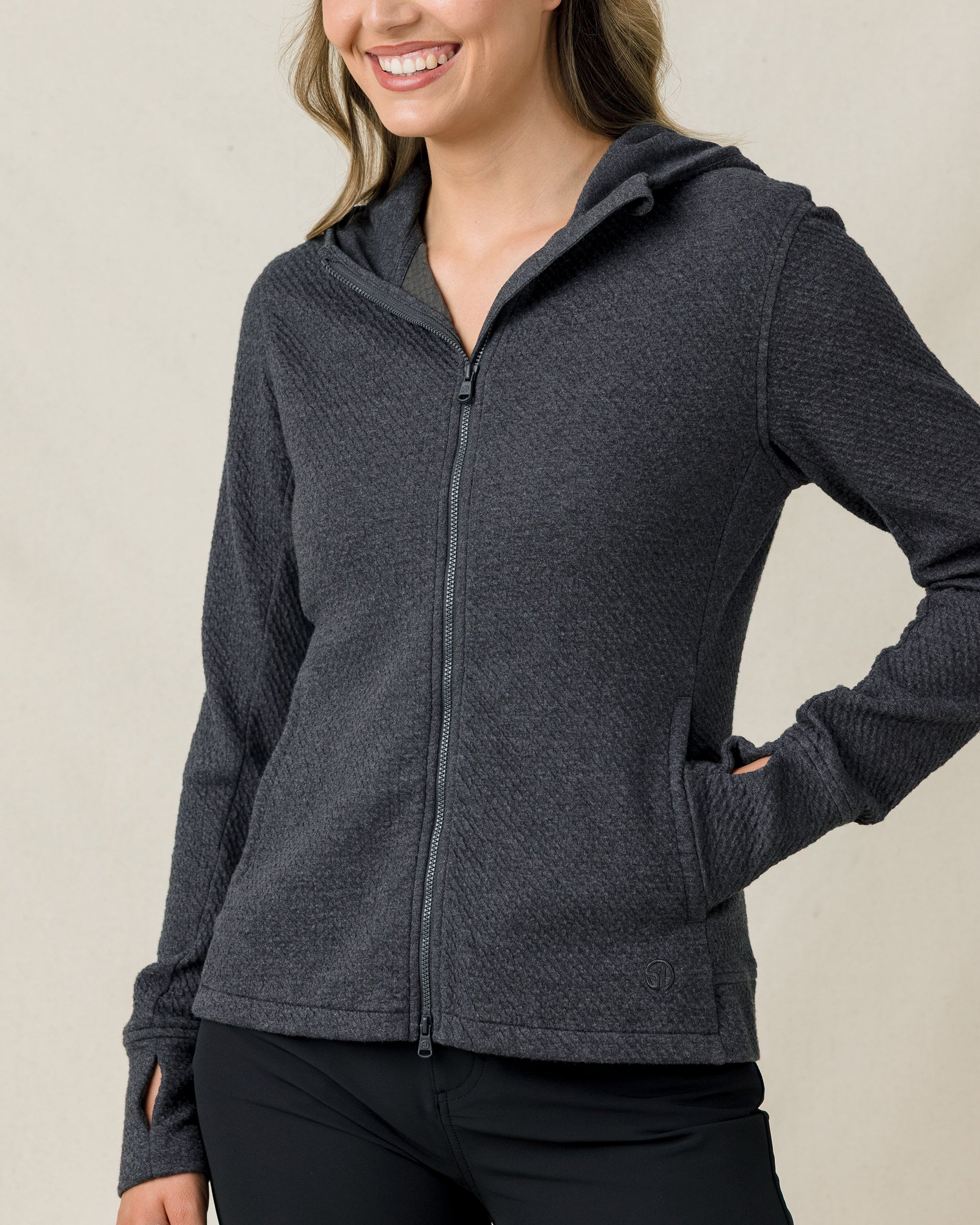 Front close-up of a woman modeling a charcoal gray textured full-zip hooded jacket with thumbhole cuffs and zippered hand pockets.