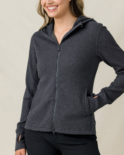 Front close-up of a woman modeling a charcoal gray textured full-zip hooded jacket with thumbhole cuffs and zippered hand pockets.