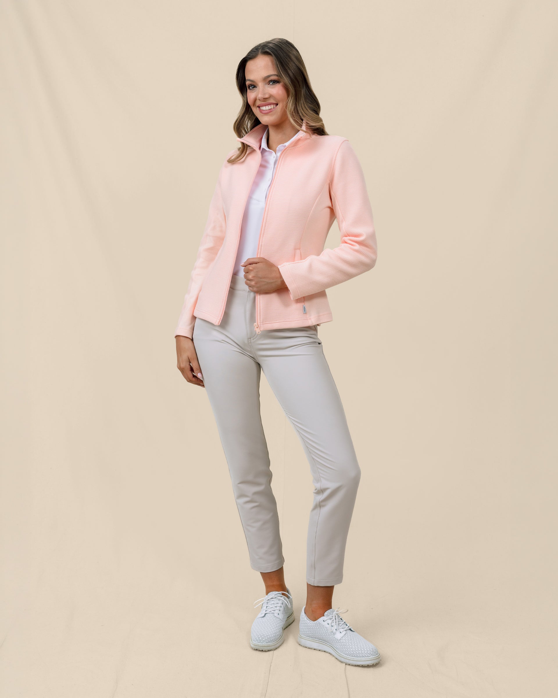 Full-length view of a model wearing the New Swing Jacket in Melba open over a white polo with light-colored pants and golf shoes.