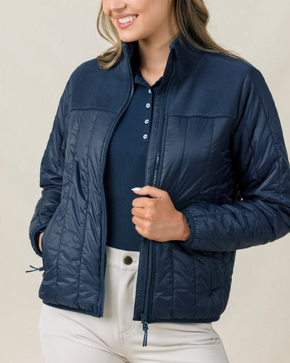 Woman wearing the Taylor Jacket in New Indigo unzipped over a navy golf polo