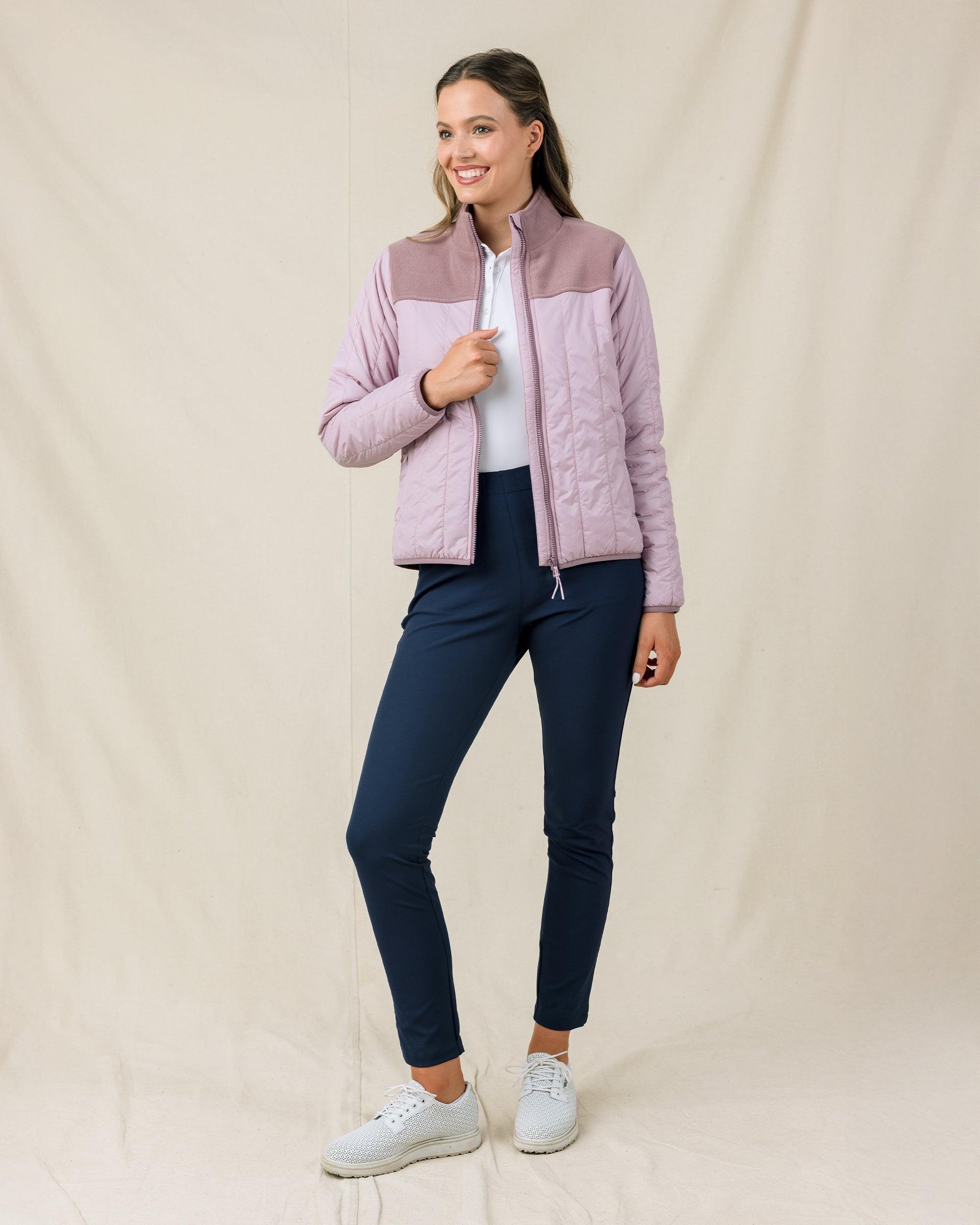 Model wearing the Taylor Jacket in Pink Dawn unzipped over a white polo with navy golf pants
