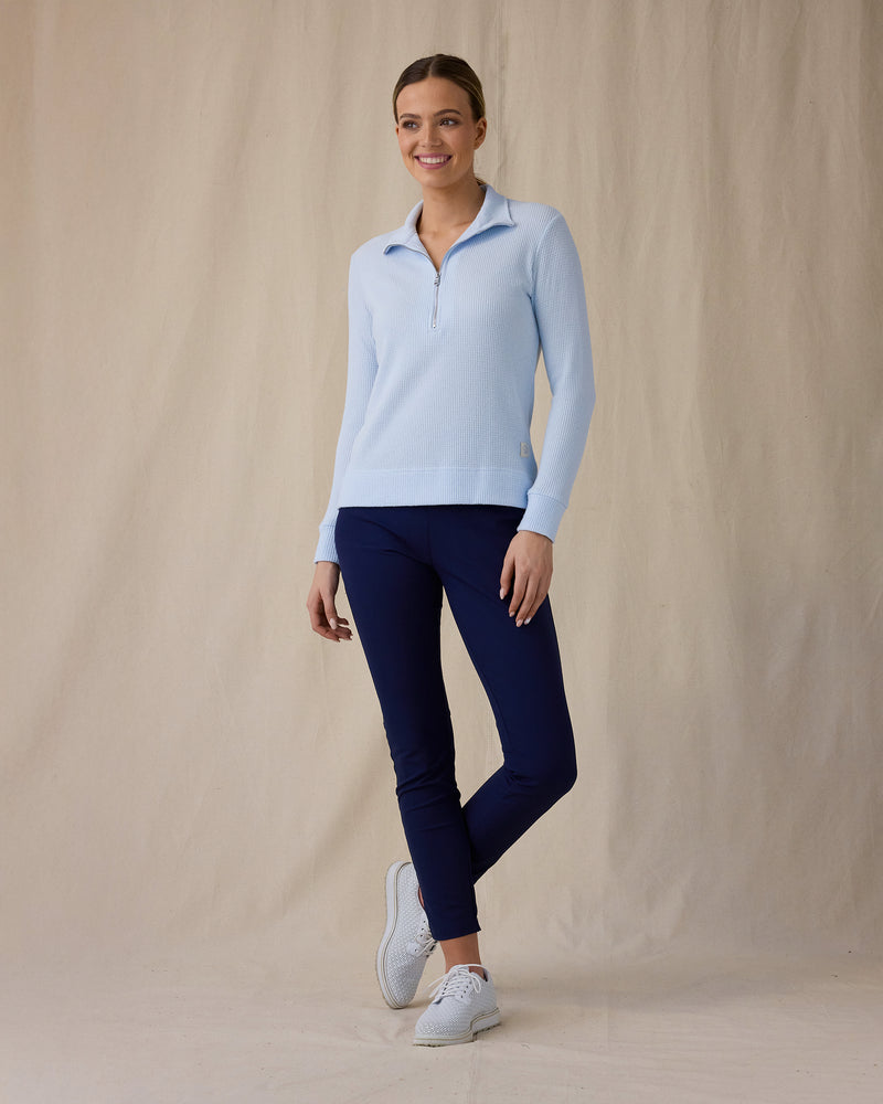 Women's Hills Quarter Zip in Lake, full length front angle view on model featuring a light blue waffle-knit quarter-zip pullover with mock neck collar and Straight Down logo patch at the hem, paired with navy pants and white golf shoes