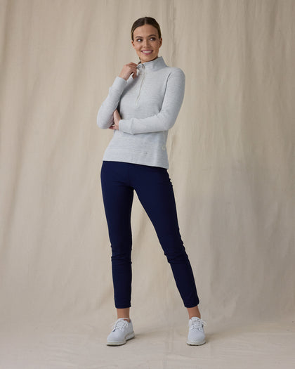 Women's Hills Quarter Zip in New Heather, front full-length view featuring a light heather gray waffle-knit quarter zip pullover with silver zipper and hand gripping zipper pull paired with navy pants and white shoes