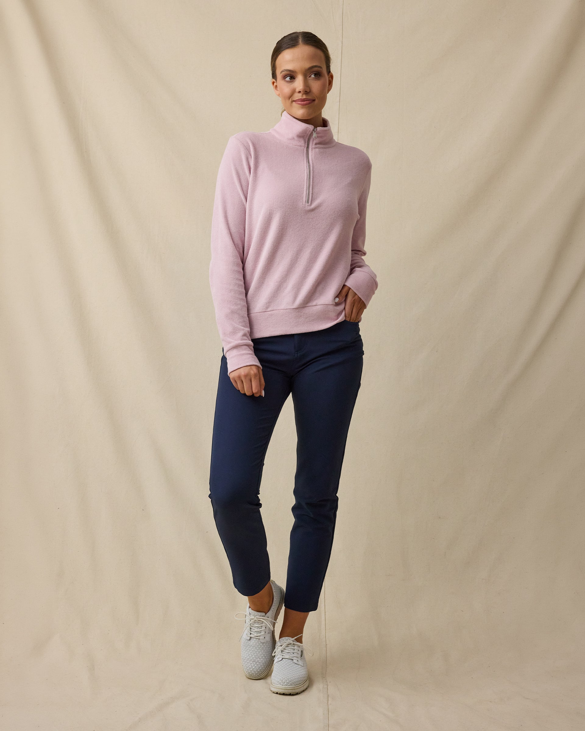 Woman wearing the Collette Quarter Zip in Pink Dawn fully zipped with navy golf pants