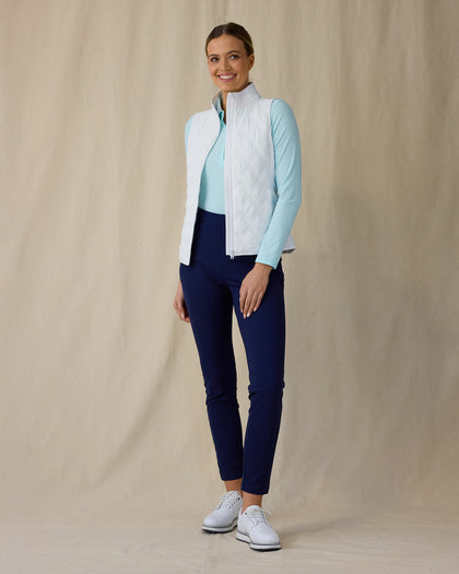 Women's Hestia Vest in White, full length front view on model featuring a white quilted diamond-pattern full-zip vest worn open over a mint long-sleeve top, paired with navy pants and white golf shoes