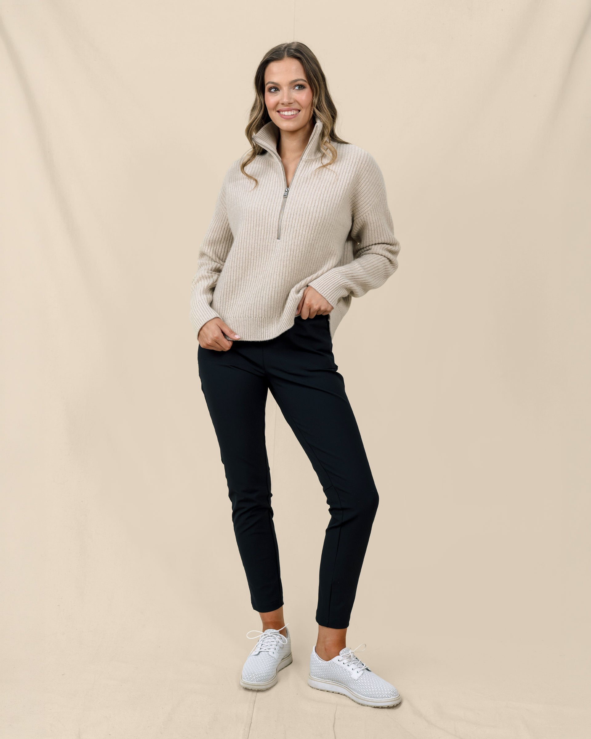 Woman wearing the Devon Half Zip Sweater in Oat with black pants and white golf shoes.