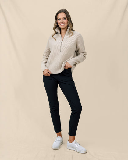 Woman wearing the Devon Half Zip Sweater in Oat with black pants and white golf shoes.
