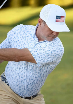 Golfer wearing the Independence Day Polo during a swing, featuring a white-and-blue patriotic print and a performance golf hat