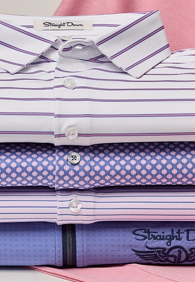 A stack of folded Straight Down dress shirts in various patterns and colors, including white with purple stripes, purple with a pink geometric pattern, and lavender with a textured print.