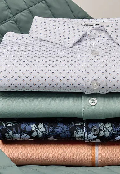 A stack of folded dress shirts displayed on a quilted green fabric surface. The top shirt is white with a small repeating geometric pattern in muted blue, green, and orange.
