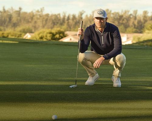 Man preparing to putt on a golf course with a crouched position.